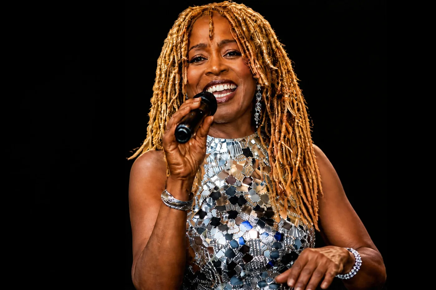 JB Rose singing into a microphone in a silver mirrored dress.